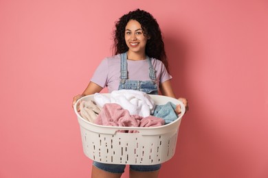 Happy woman with basket full of laundry on pink background