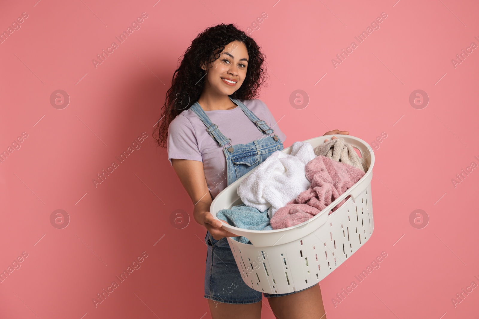 Photo of Happy woman with basket full of laundry on pink background