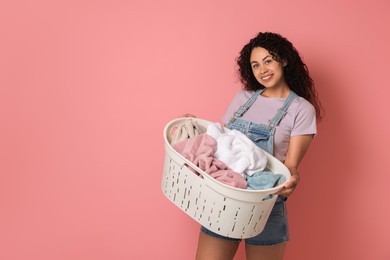 Photo of Happy woman with basket full of laundry on pink background, space for text