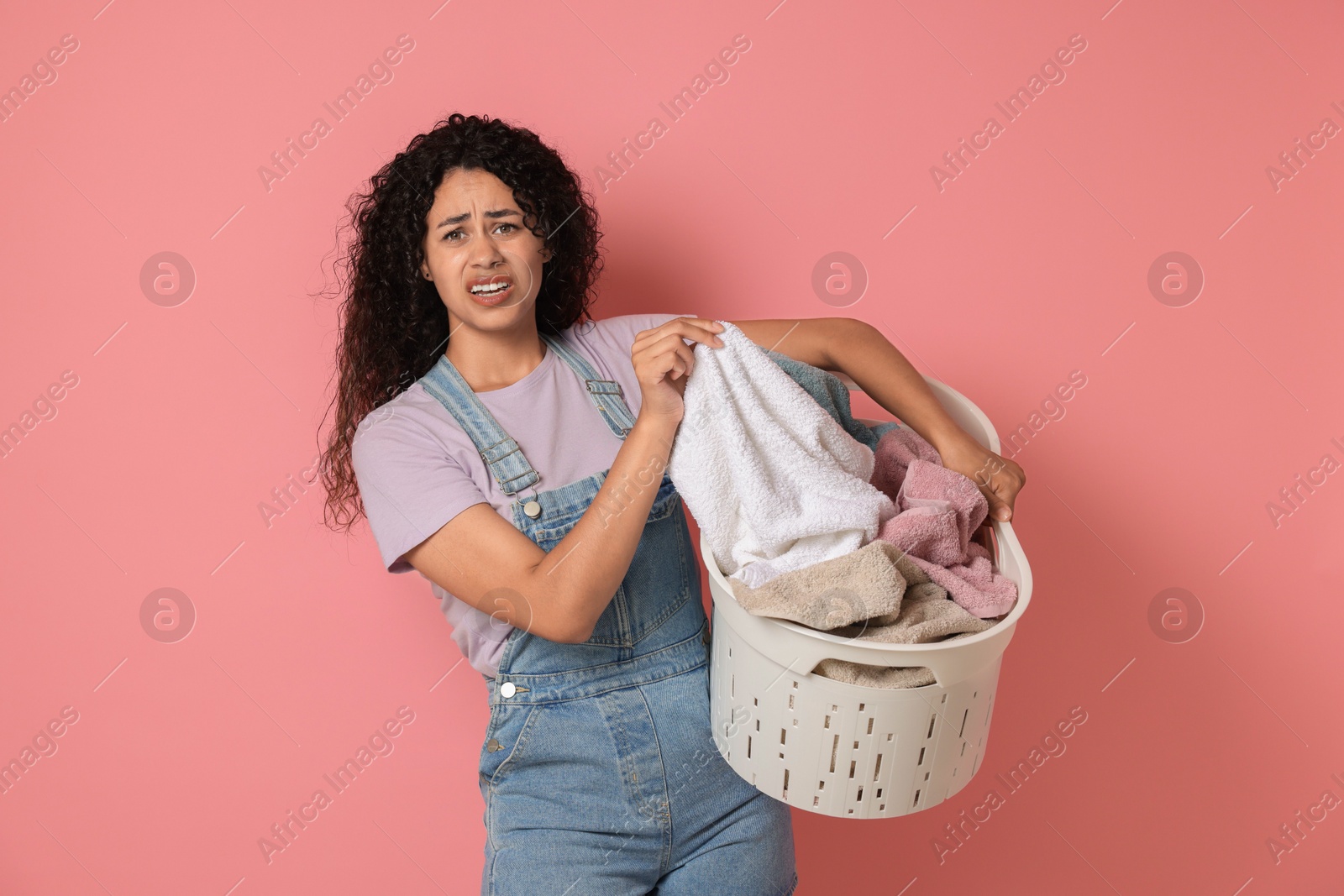 Photo of Displeased woman with basket full of laundry on pink background