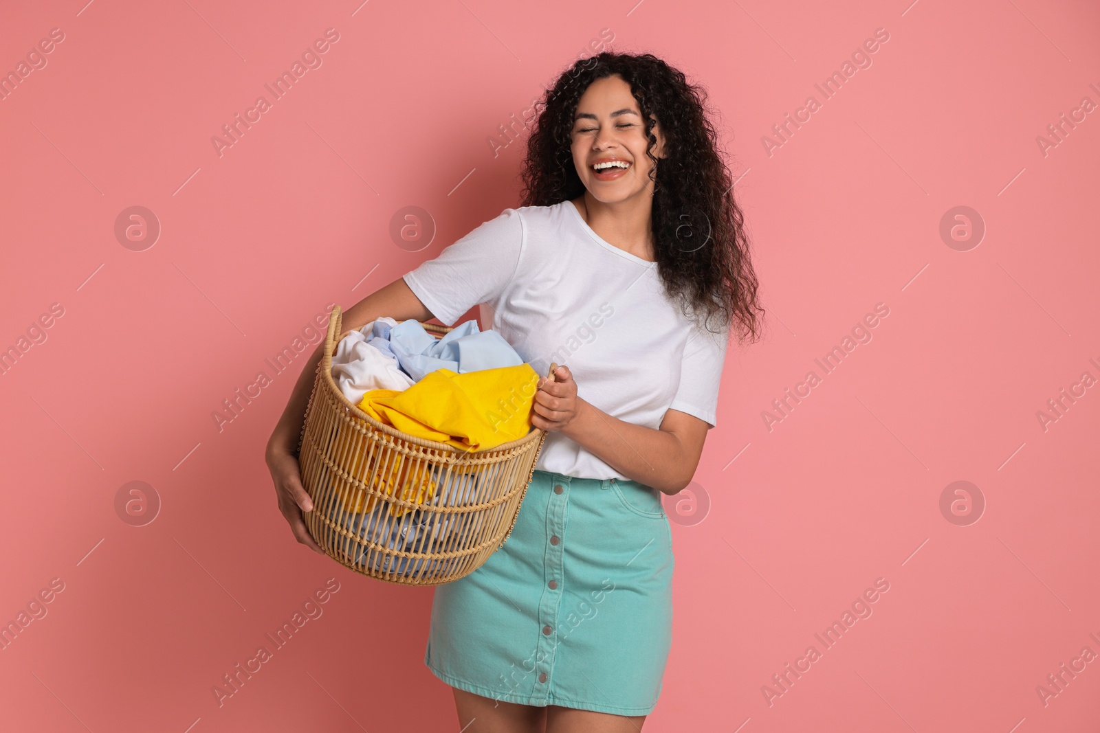 Photo of Happy woman with basket full of laundry on pink background