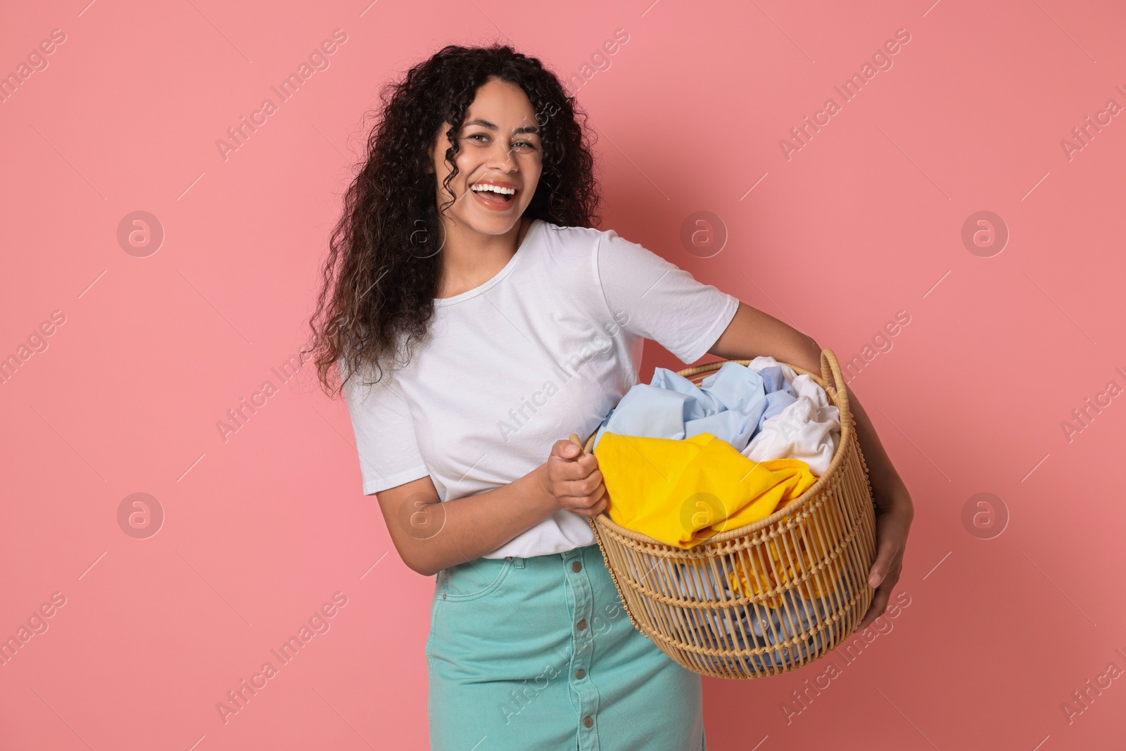 Photo of Happy woman with basket full of laundry on pink background