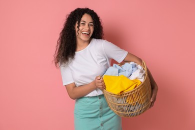 Happy woman with basket full of laundry on pink background