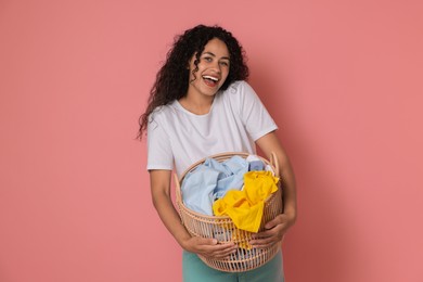 Photo of Happy woman with basket full of laundry on pink background