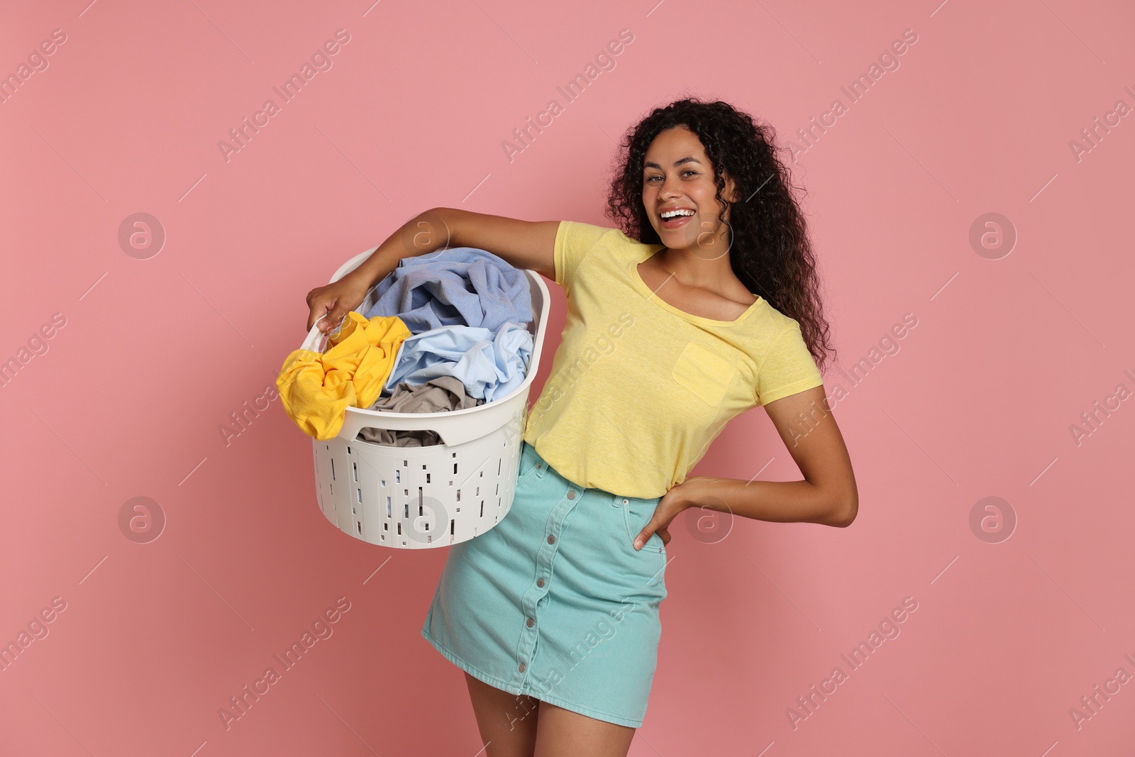 Photo of Happy woman with basket full of laundry on pink background