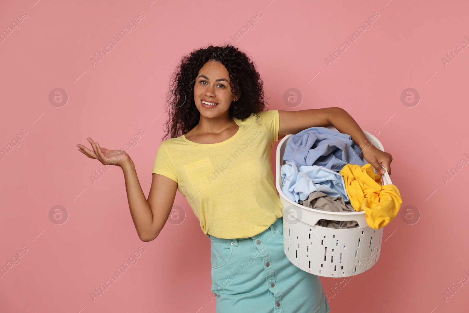 Photo of Happy woman with basket full of laundry on pink background