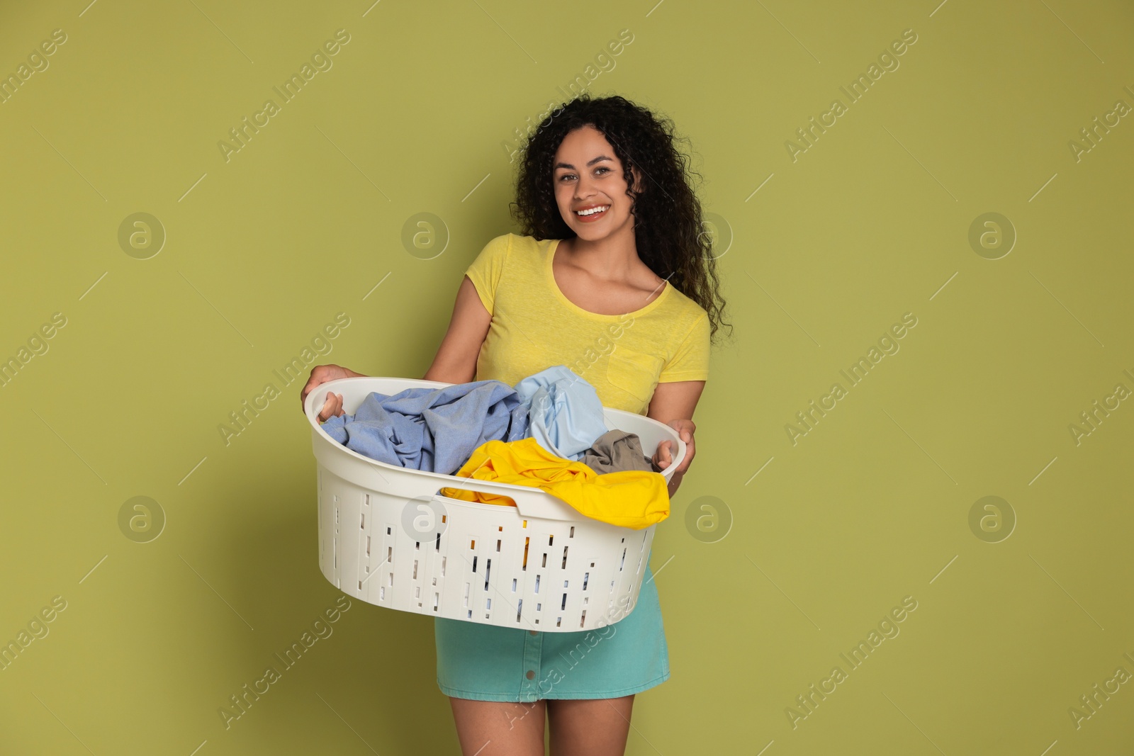 Photo of Happy woman with basket full of laundry on olive background