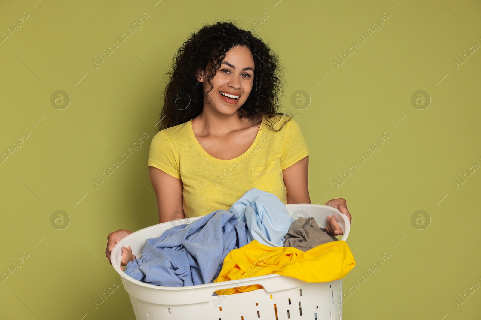 Photo of Happy woman with basket full of laundry on olive background