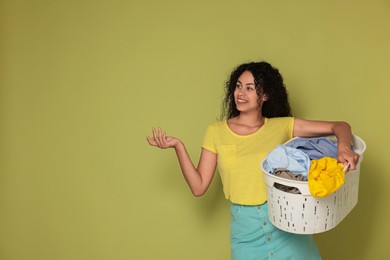 Happy woman with basket full of laundry on olive background, space for text