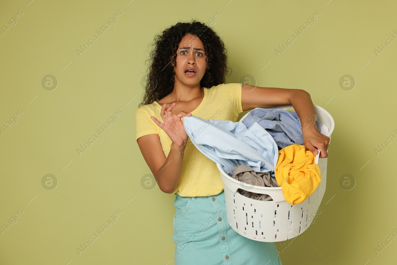 Photo of Displeased woman with basket full of laundry on olive background, space for text