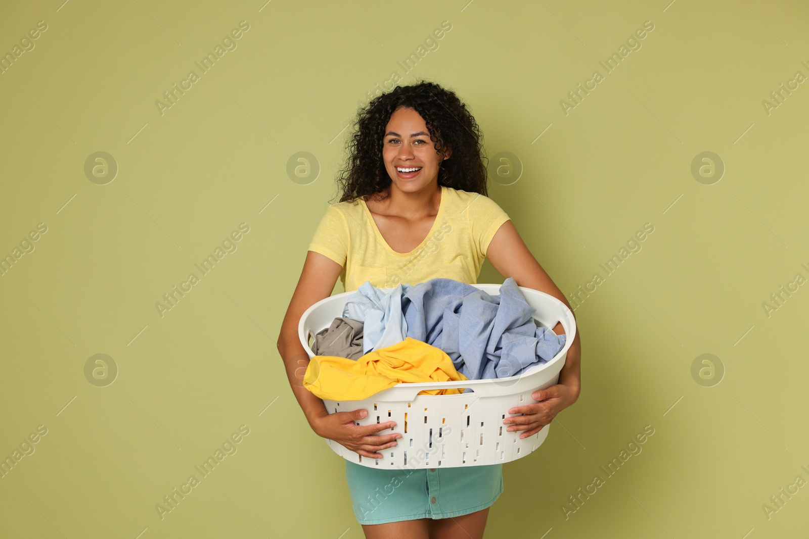 Photo of Happy woman with basket full of laundry on olive background