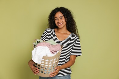 Happy woman with basket full of laundry on olive background