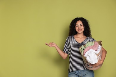 Photo of Happy woman with basket full of laundry on olive background, space for text