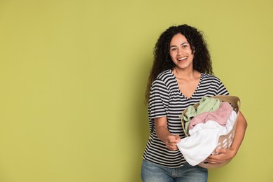 Photo of Happy woman with basket full of laundry on olive background, space for text