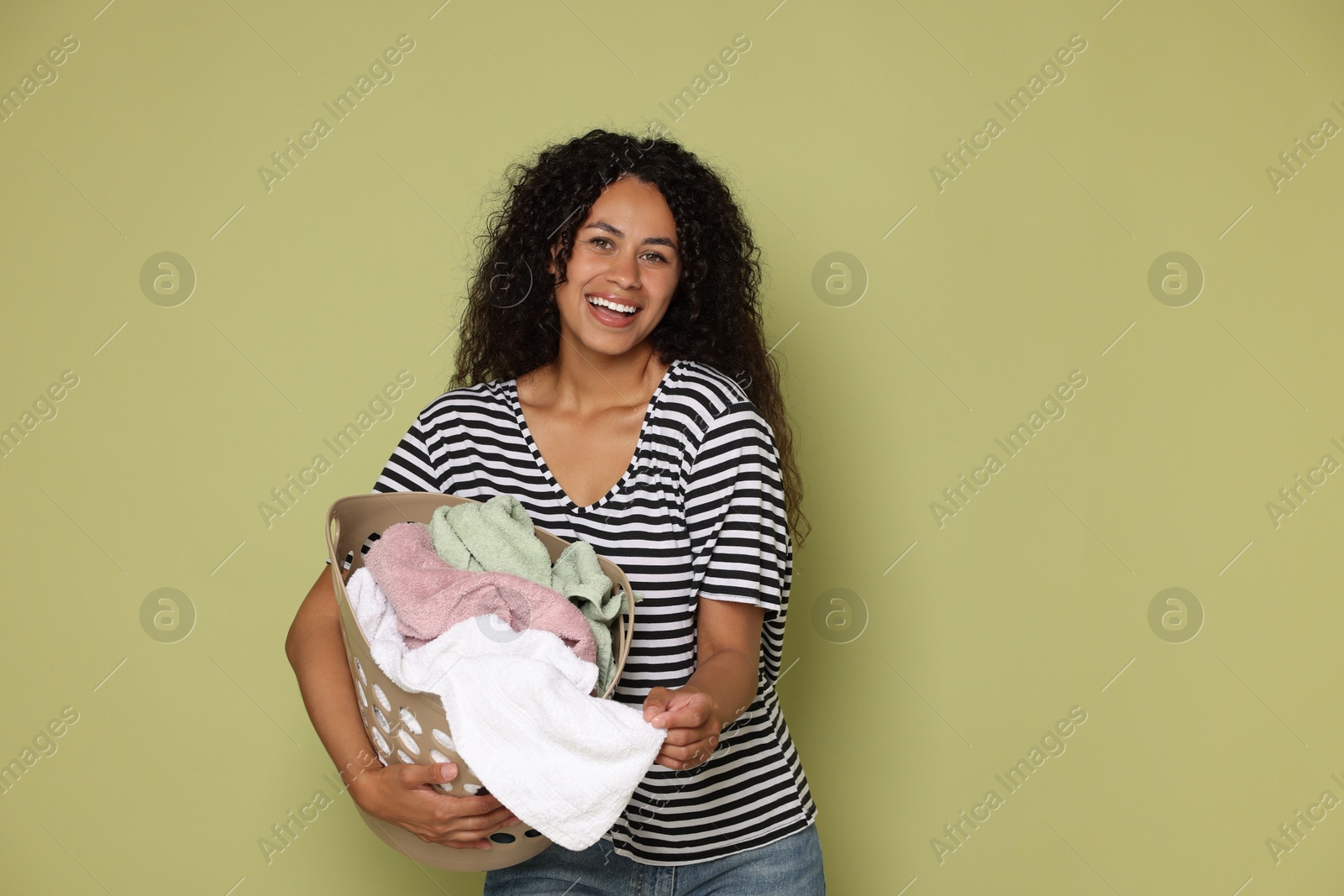 Photo of Happy woman with basket full of laundry on olive background, space for text