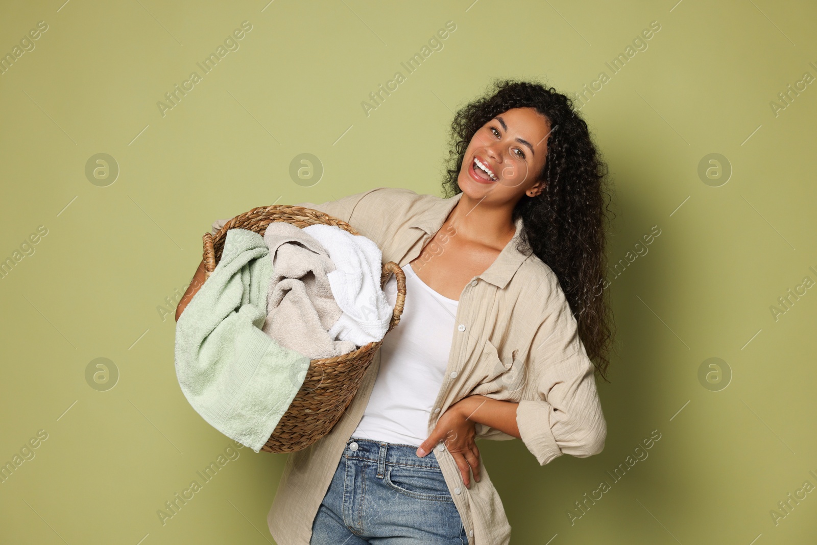 Photo of Happy woman with basket full of laundry on olive background