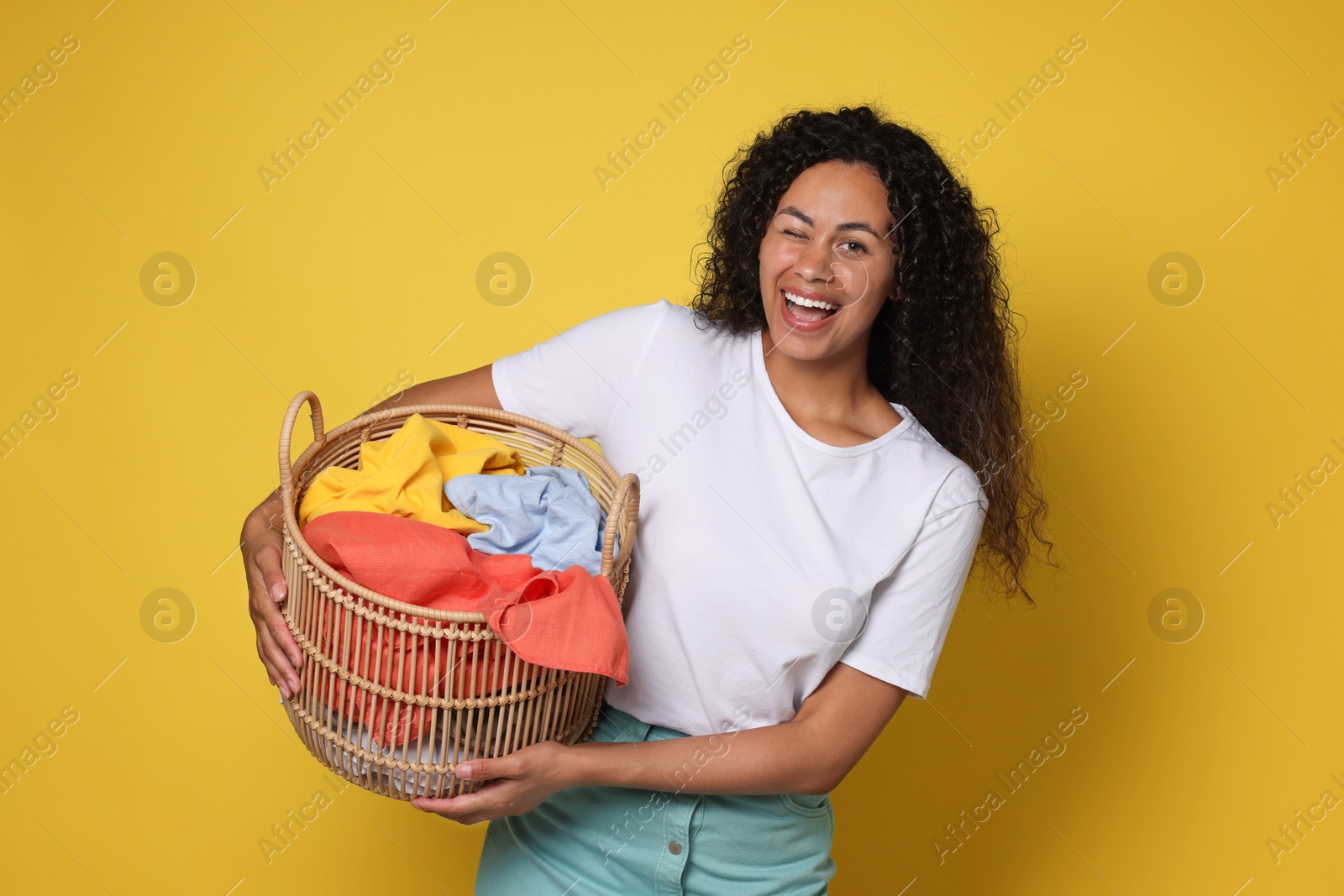 Photo of Happy woman with basket full of laundry on yellow background