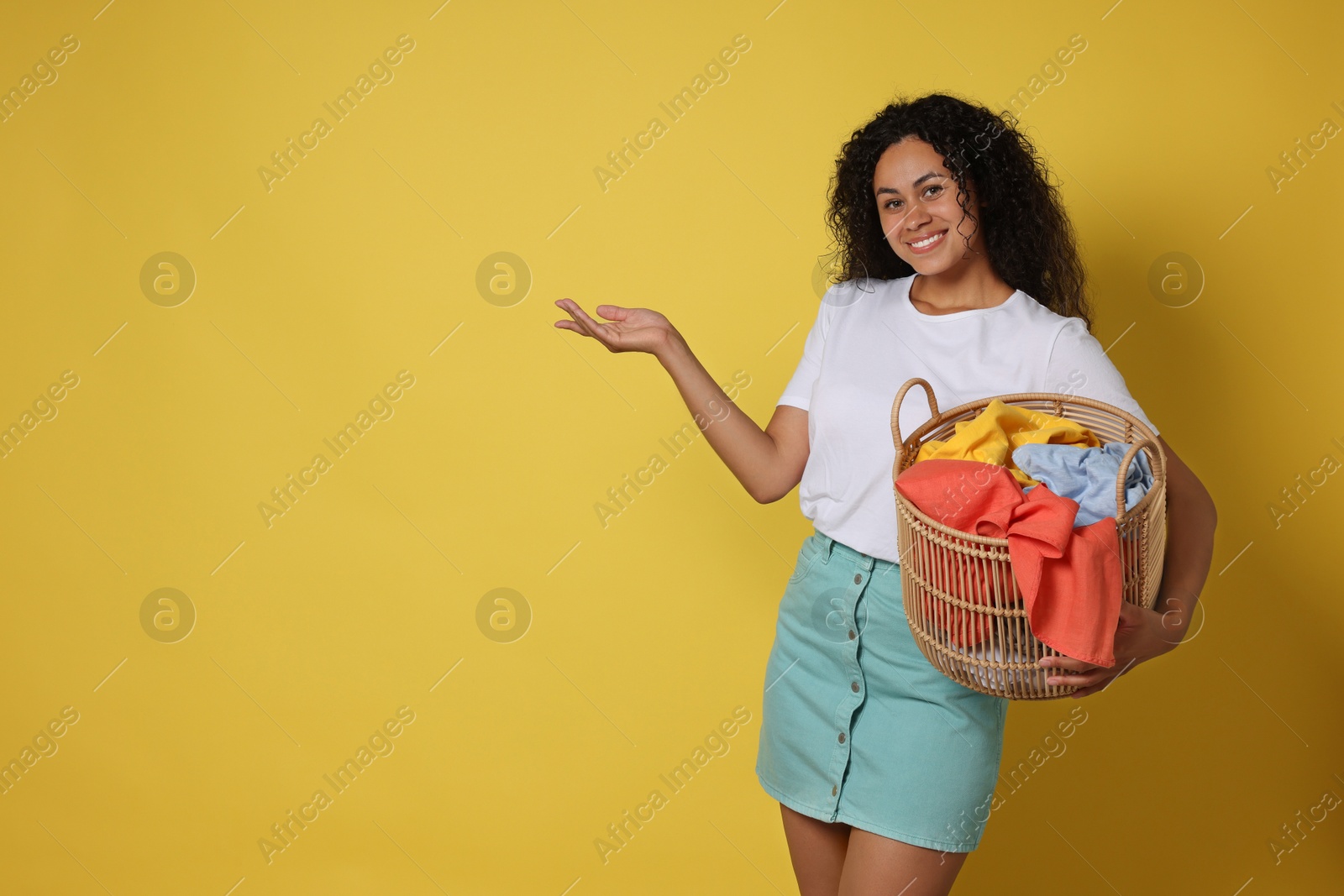 Photo of Happy woman with basket full of laundry on yellow background, space for text