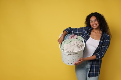 Happy woman with basket full of laundry on yellow background, space for text