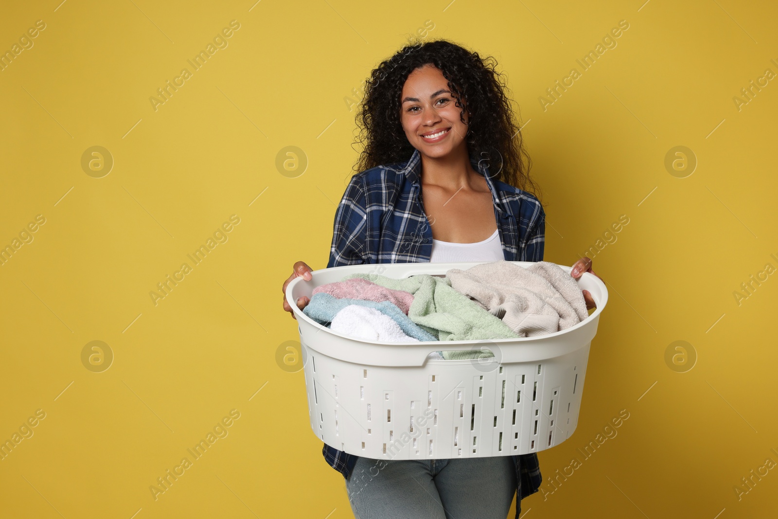 Photo of Happy woman with basket full of laundry on yellow background, space for text