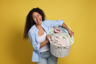 Photo of Happy woman with basket full of laundry on yellow background