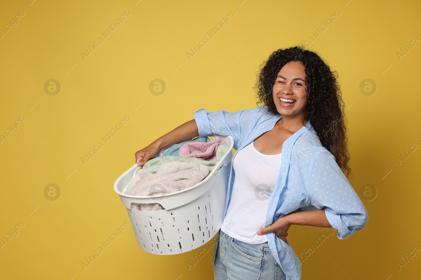 Photo of Happy woman with basket full of laundry on yellow background, space for text