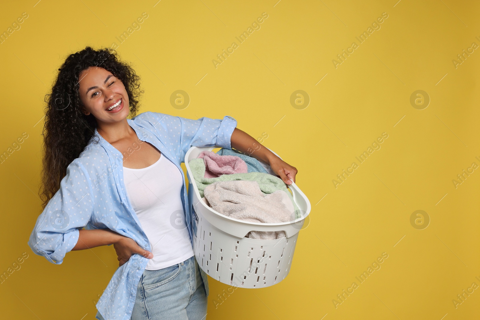 Photo of Happy woman with basket full of laundry on yellow background, space for text