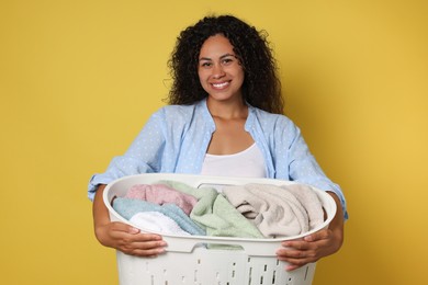 Photo of Happy woman with basket full of laundry on yellow background