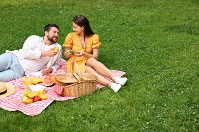 Lovely couple having picnic on green grass outdoors. Space for text