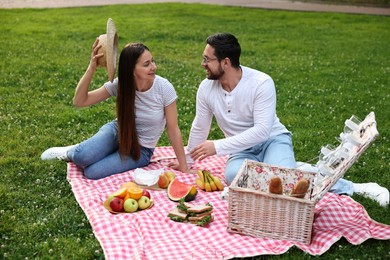 Photo of Happy couple having picnic on green grass outdoors