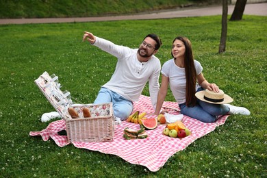 Romantic picnic. Smiling man pointing at something to his girlfriend on green grass outdoors