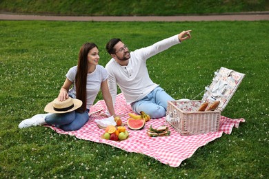 Romantic picnic. Smiling man pointing at something to his girlfriend on green grass outdoors