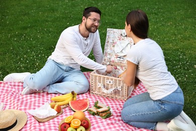 Photo of Happy couple having picnic on green grass outdoors