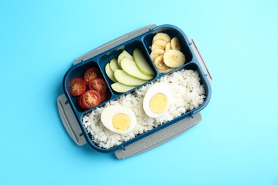 Photo of Lunch box with rice, fruits, tomatoes and egg halves on light blue background, top view