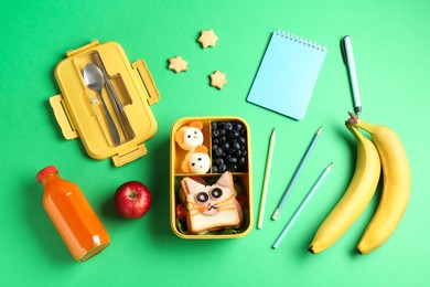 Photo of Lunch box with snacks, bottle of juice, cutlery and stationery on green table, flat lay