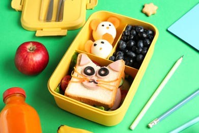 Photo of Lunch box with snacks, bottle of juice and pencils on green table, closeup