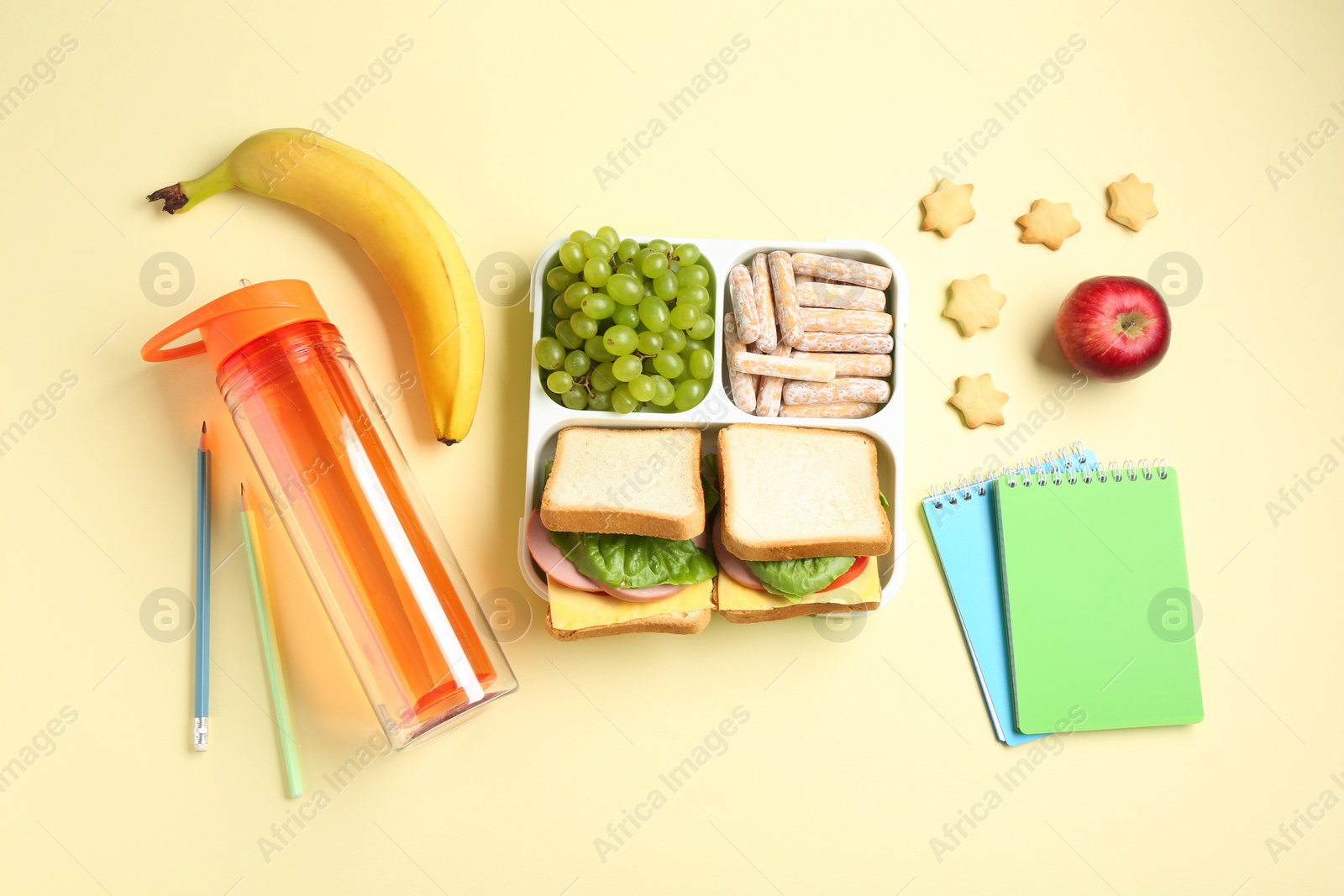 Photo of Lunch box with snacks, bottle and stationery on yellow table, flat lay