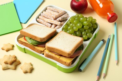 Photo of Lunch box with snacks, bottle of juice and stationery on yellow table, closeup