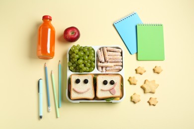 Photo of Sandwiches with smiley faces in lunch box, bottle of juice and stationery on yellow table, flat lay