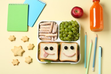 Photo of Sandwiches with smiley faces in lunch box, bottle of juice and stationery on yellow table, flat lay