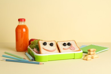 Photo of Sandwiches with smiley faces in lunch box, bottle of juice and stationery on yellow table