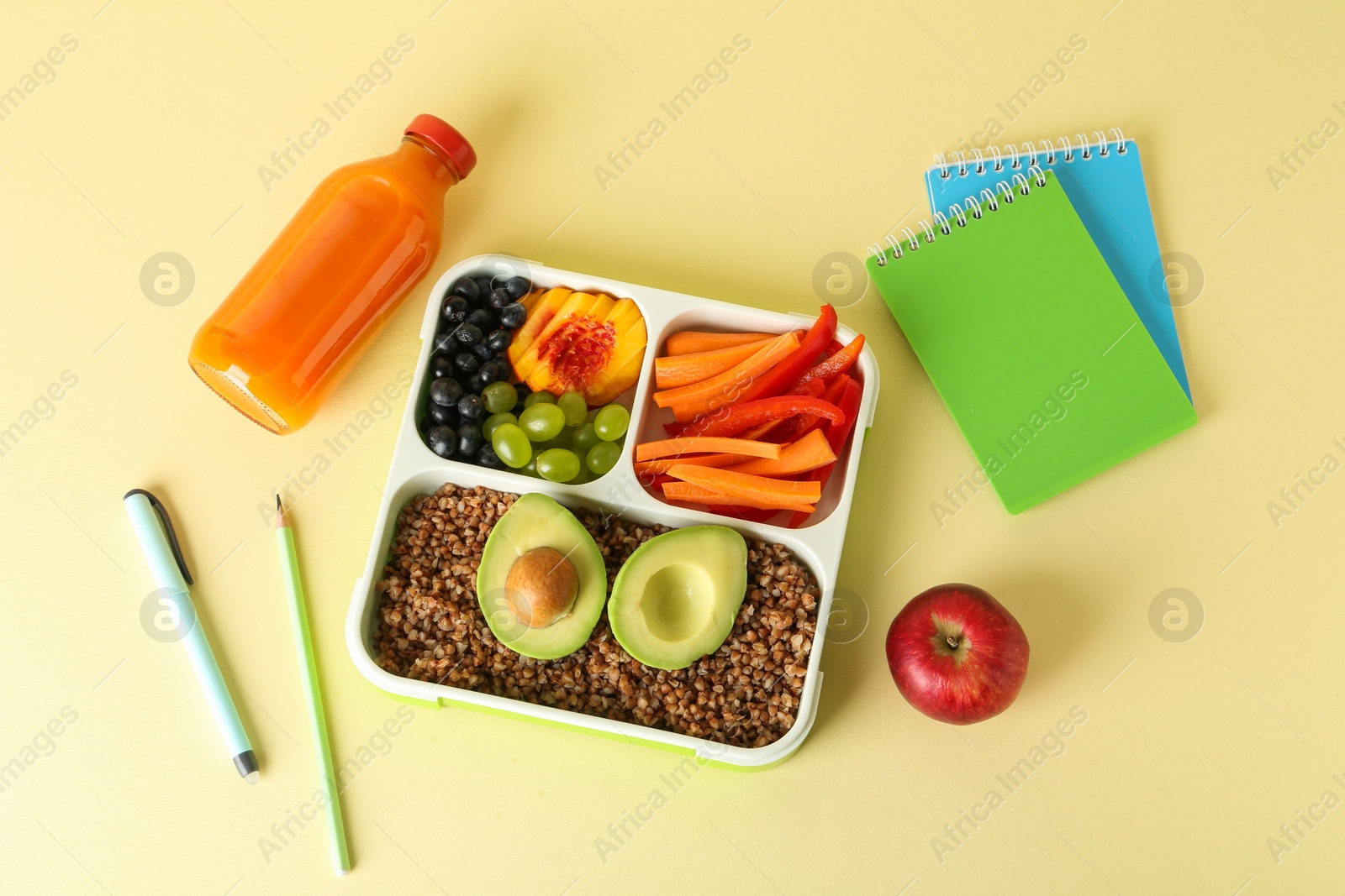 Photo of Lunch box with snacks, bottle of juice and stationery on yellow table, flat lay