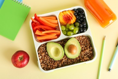 Photo of Lunch box with snacks, bottle of juice and stationery on yellow table, flat lay