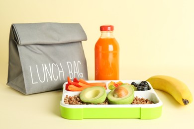 Photo of Gray bag, lunch box with snacks and bottle of juice on yellow background