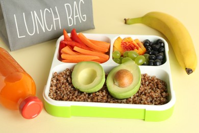 Photo of Gray bag, lunch box with snacks and bottle of juice on yellow table, closeup