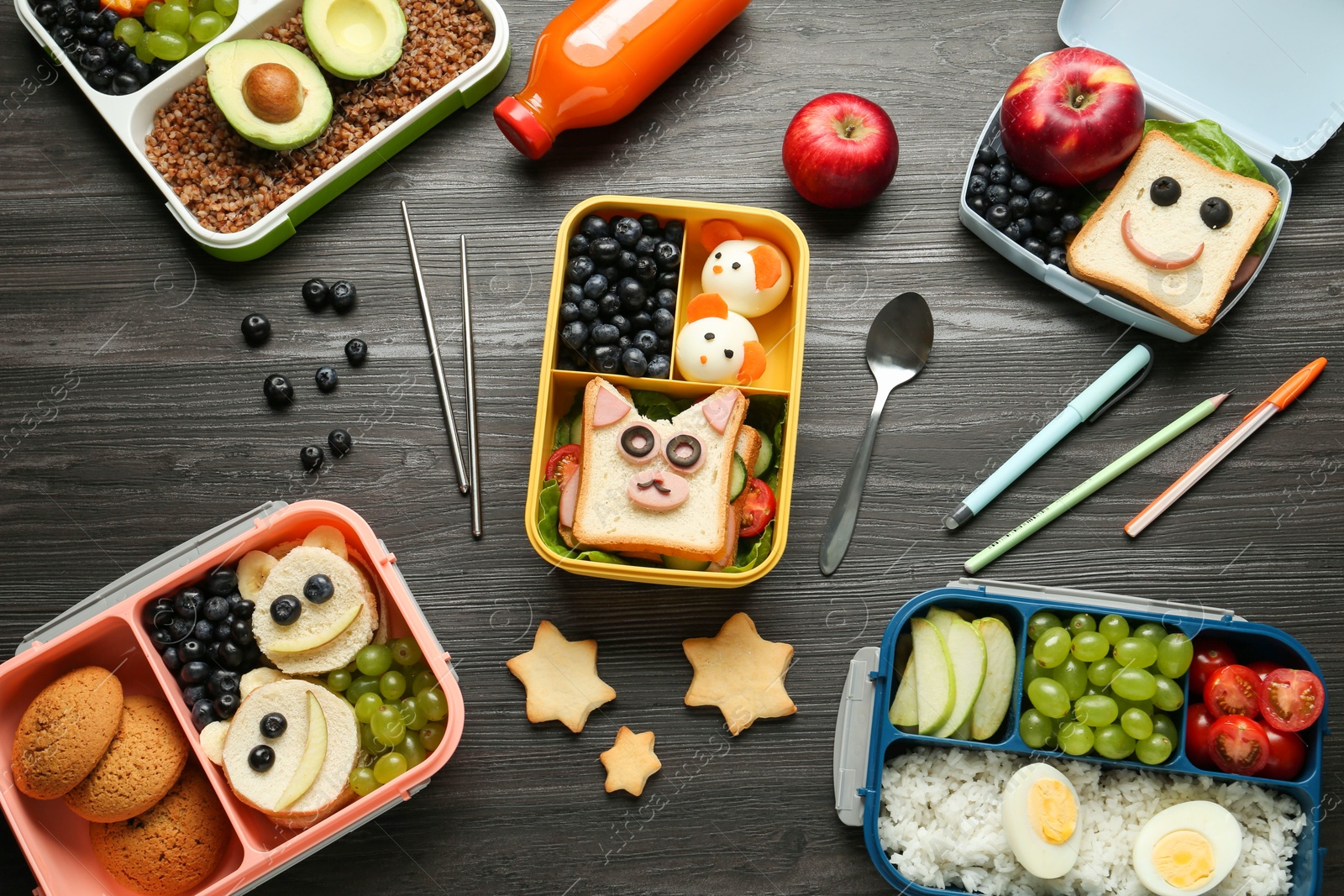 Photo of Lunch boxes with different snacks, bottle of juice and cutlery on wooden table, flat lay