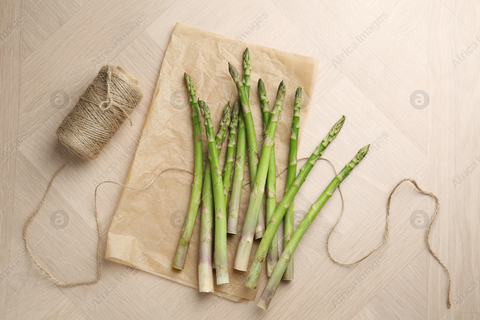 Photo of Fresh green asparagus stems and thread on wooden table, flat lay