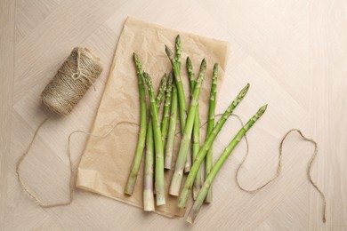 Photo of Fresh green asparagus stems and thread on wooden table, flat lay