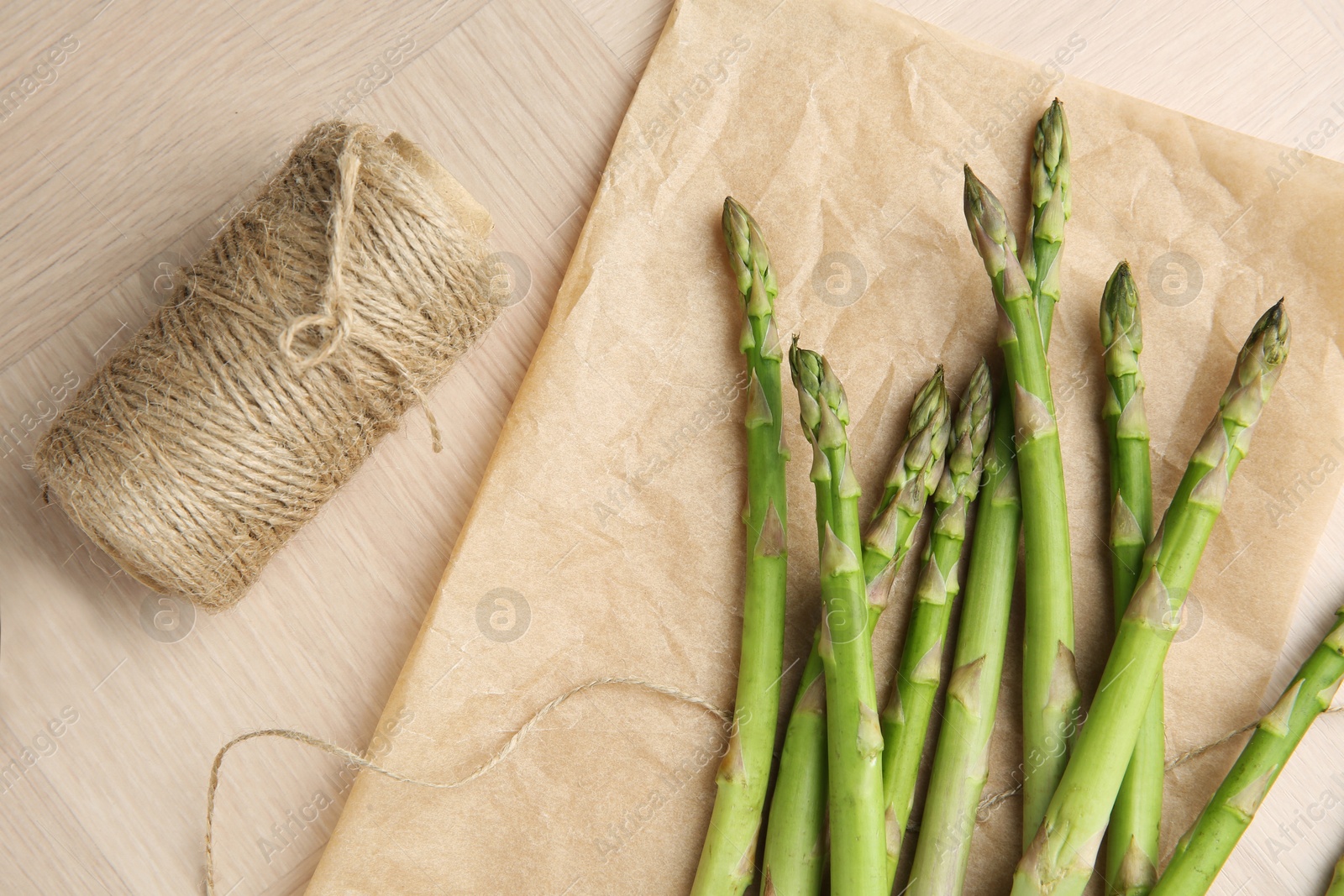 Photo of Fresh green asparagus stems and thread on wooden table, flat lay