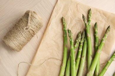 Photo of Fresh green asparagus stems and thread on wooden table, flat lay